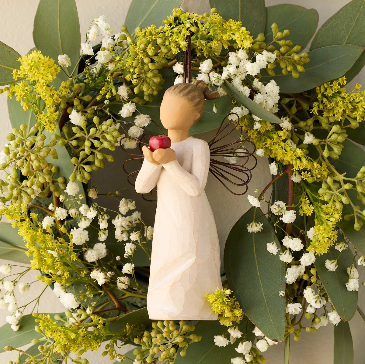 Willow Tree You're the Best! Ornament, 4.5"h hand-painted resin figure in cream dress with wire wings, holding red apple, brown elastic cord, hanging inside spring wreath