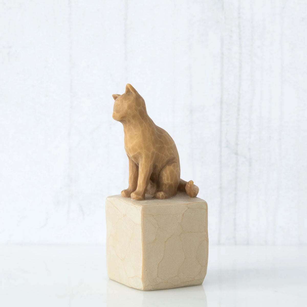 Figure of orange cat with tilted head perched atop a cream colored rectangular pedestal, facing left