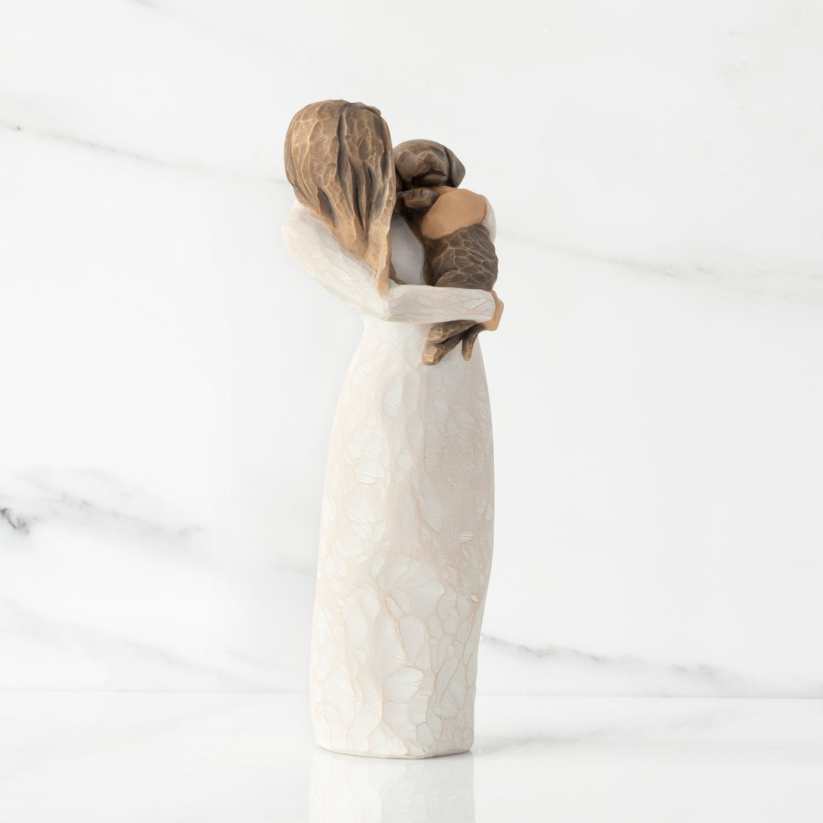 Right view, standing female figure in cream dress, holding dark color puppy in her arms
