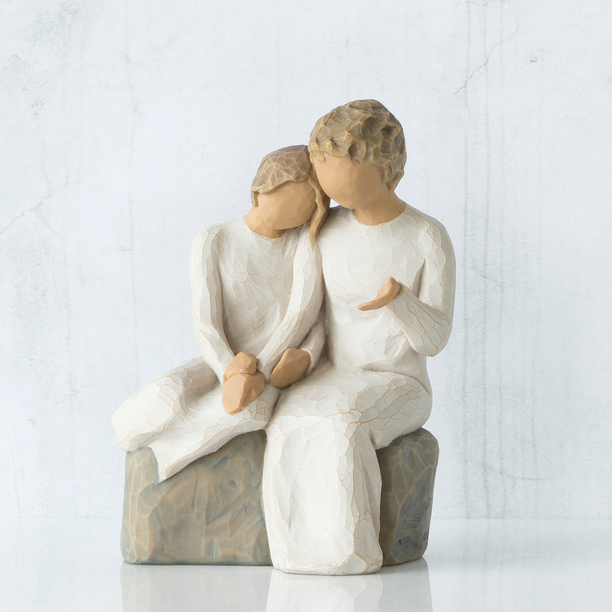 Two faceless figurines wearing white sitting next to each other on rock