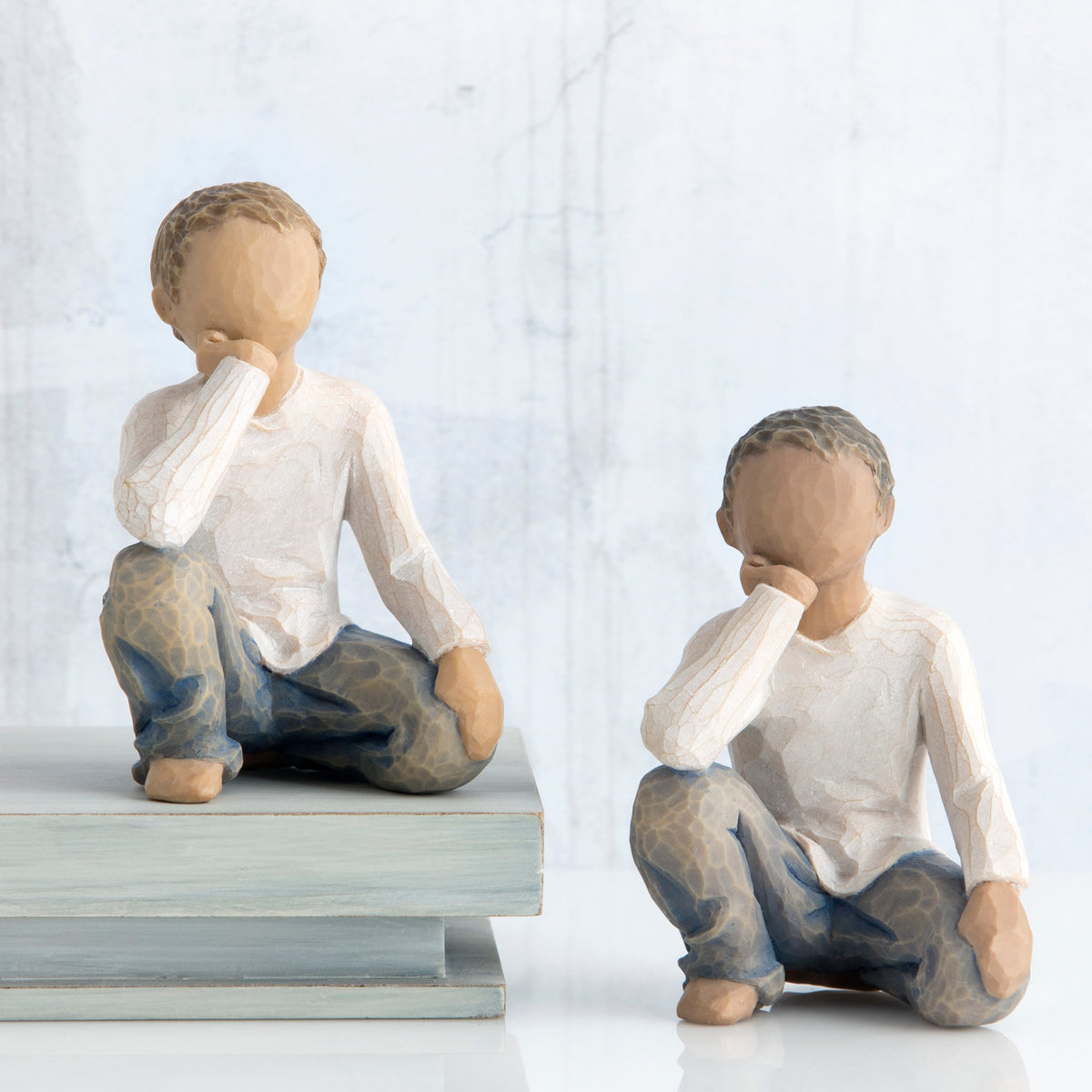 Set of two boy figurines in white shirts and blue jeans with their hands on their face