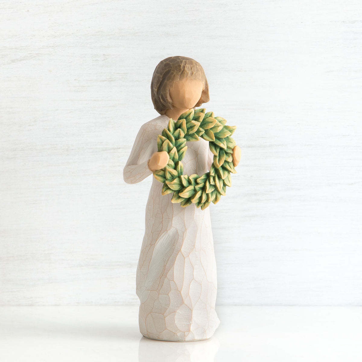 Front view of young girl with bangs and short brown hair holding up a green, leafy wreath