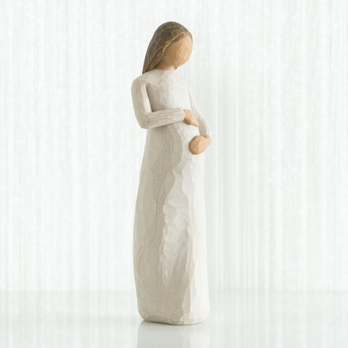 Faceless pregnant woman figurine wearing white dress with hands clutching her stomach