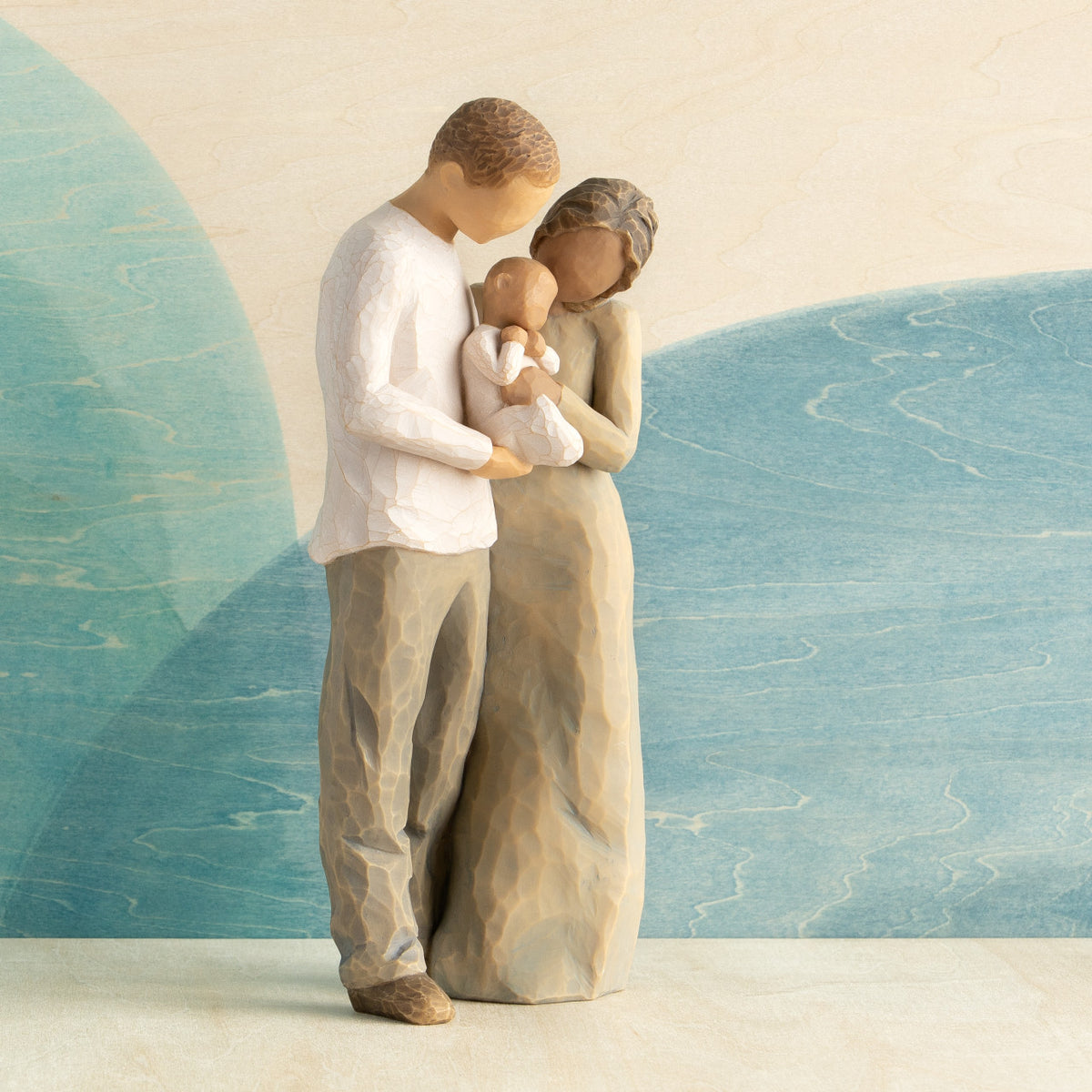 Front view of standing couple, woman has darker skin and hair; man has lighter skin and hair, holding a baby between them. Blue painted background.