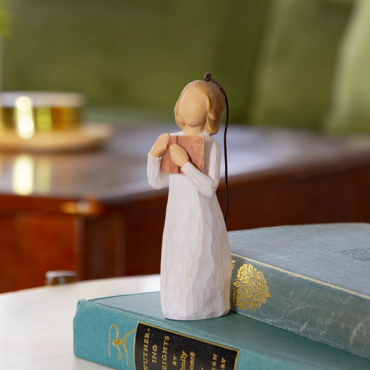 Willow Tree Love of Learning Ornament, 4”h hand-painted resin figure in cream dress holding open book to her chest, brown elastic cord, standing on pile of books