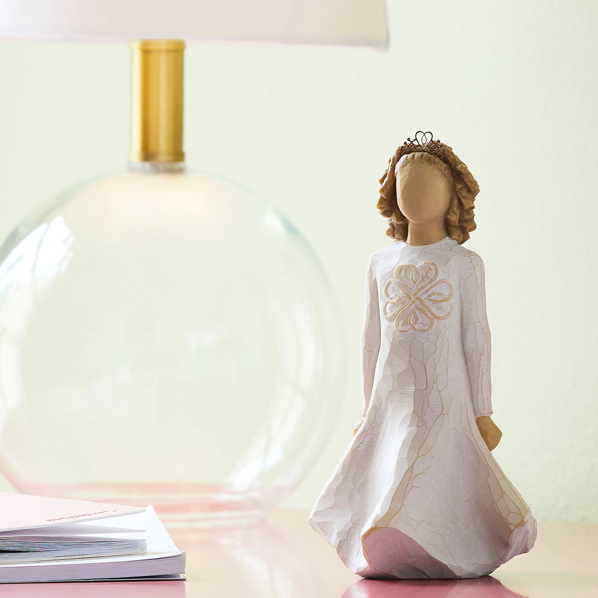 Willow Tree Irish Charm, 5.5" hand-painted dancing resin figure in cream dress with full skirt carved with stylized Celtic knot, arms down to sides, wire crown of hearts, on table with glass lamp