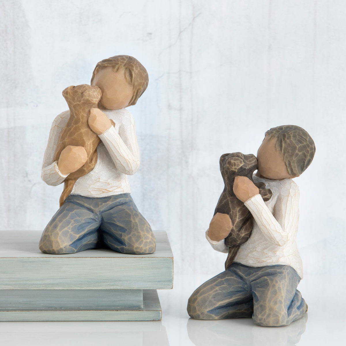 Set of two boy figurines sitting in blue jeans and white shirts holding puppy figurines