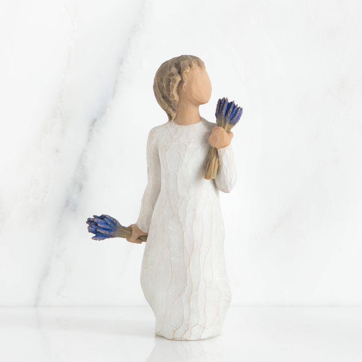 Small girl figurine wearing white dress holding two blue flower bouquets in each hand