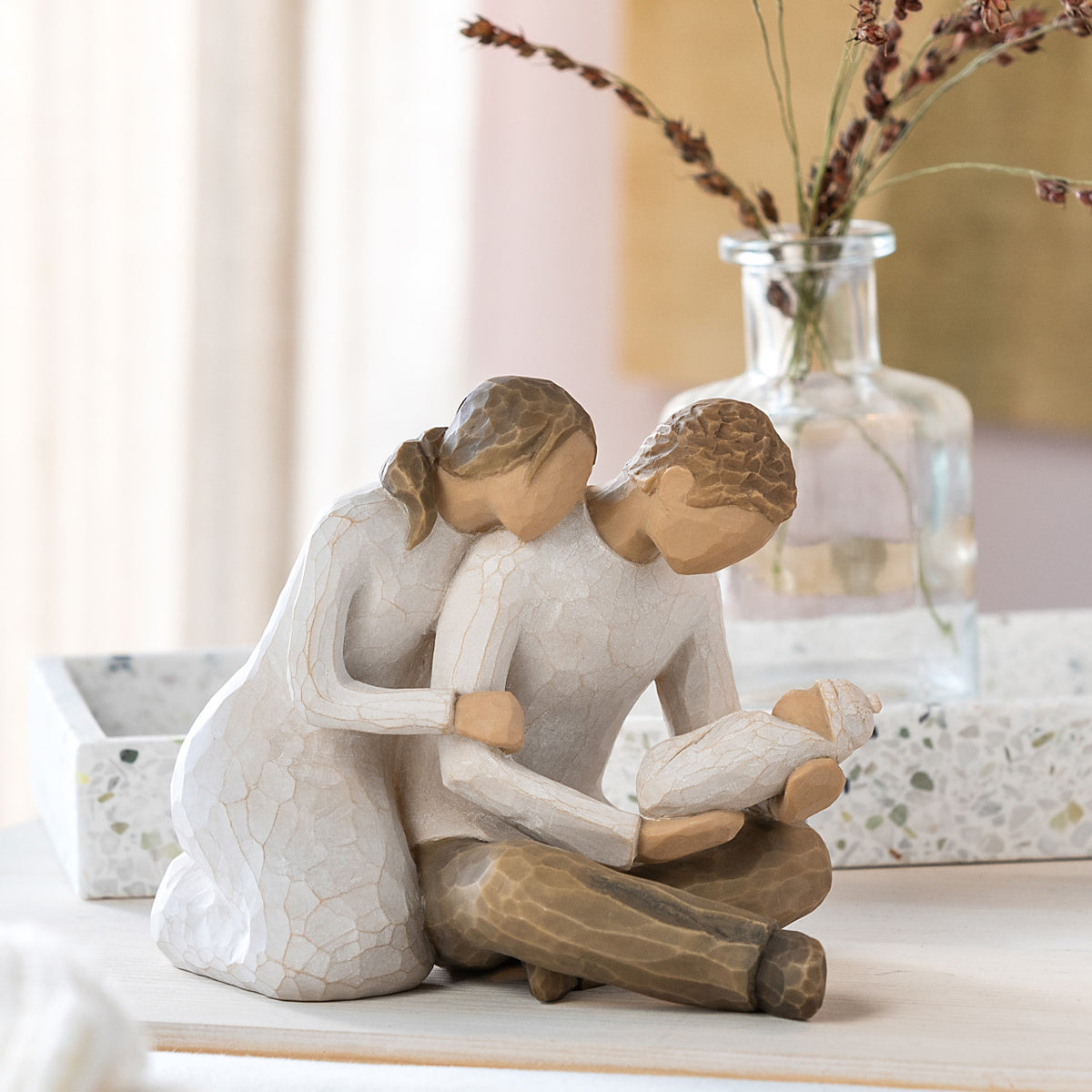 Willow Tree New Life, 5”h hand-painted resin figure of seated couple in neutral colors, holding newborn baby wrapped in cream blanket, on bedroom dresser