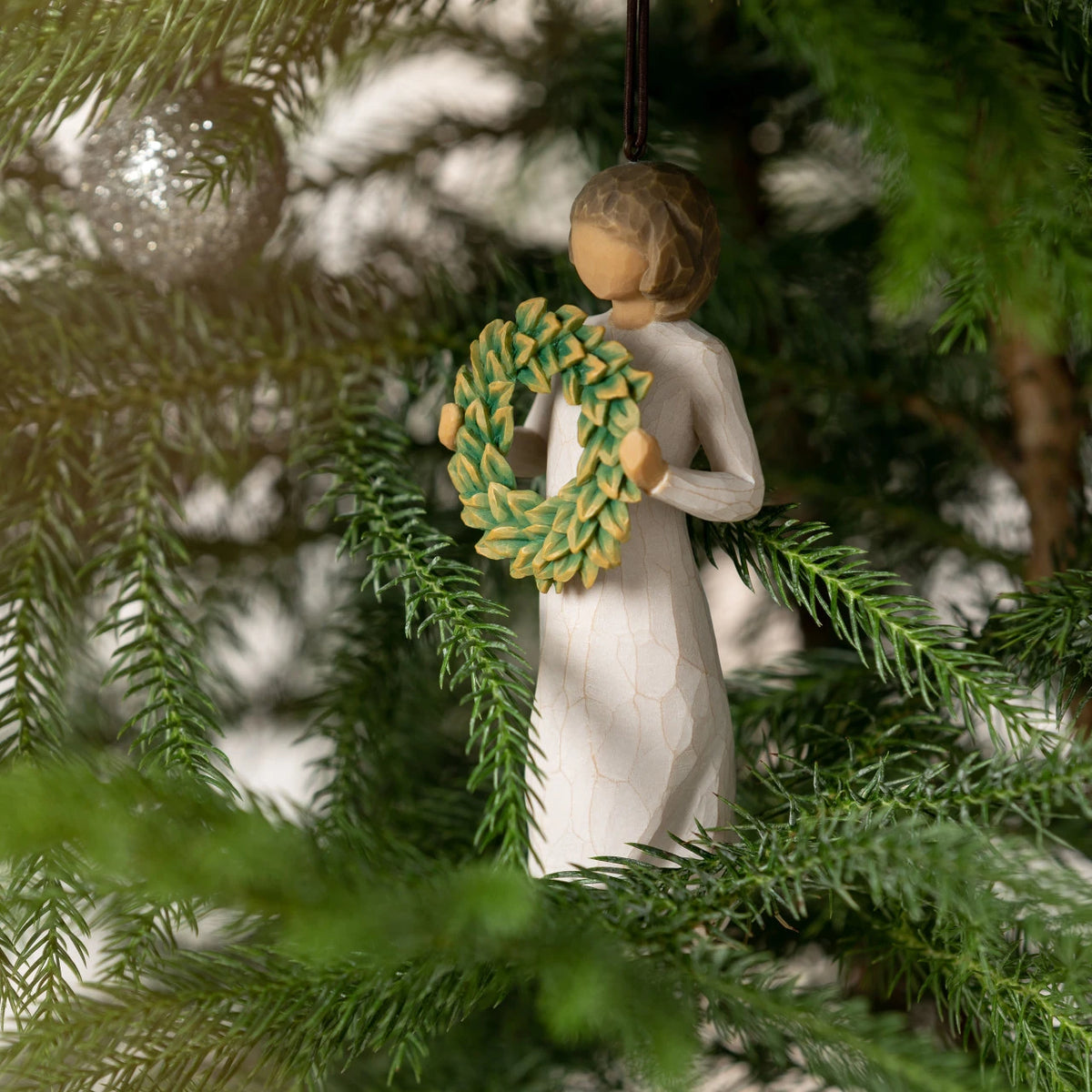 Willow Tree Magnolia Ornament, 4.25”h hand-painted resin figure in cream dress, holding green magnolia leaf wreath, brown elastic cord, nestled into tree branches