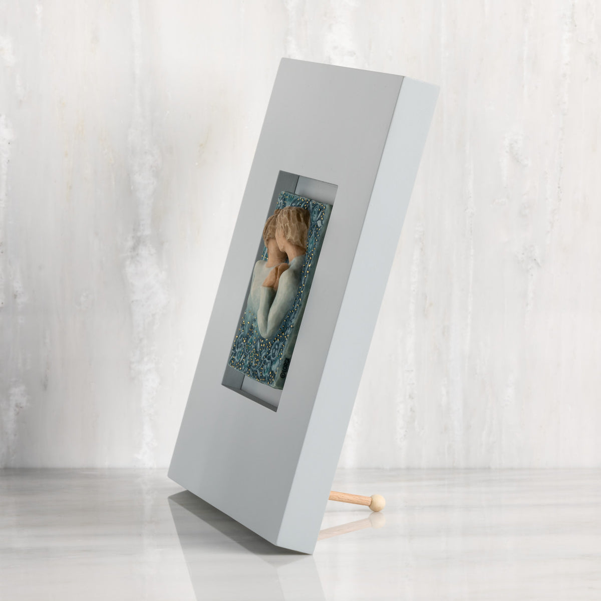 Side View: gray wood frame with inset carved plaque of embracing couple, painted in blue ombre and gold dots