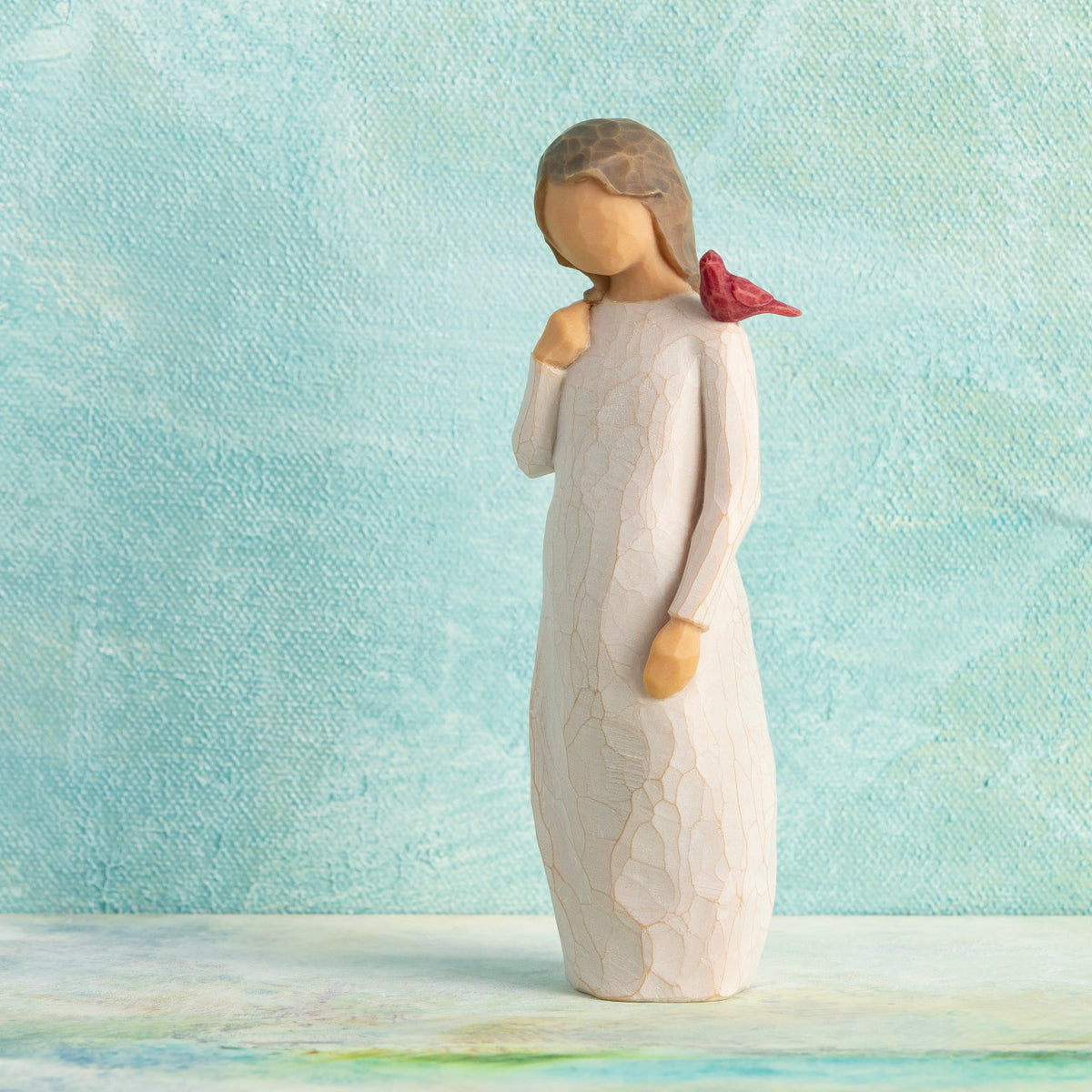 Willow Tree Messenger, 5.5”h hand-painted standing resin figure in cream dress with red cardinal perched on shoulder, in front of light teal painting