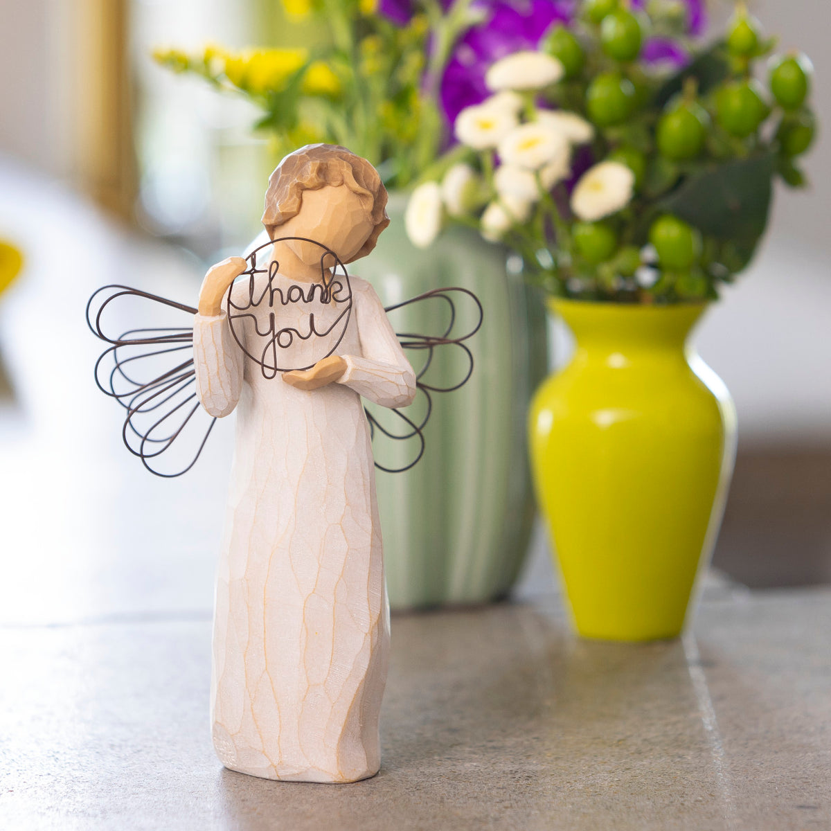 Willow Tree Just for You, 5.5”h hand-painted standing resin angel figure in cream dress with wire wings, holding wire circle with 'thank you' written in wire, on table with green florals