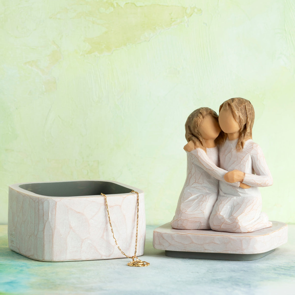 Willow Tree Sister mine Keepsake Box, 3"sq hand-painted resin box with 3.5”H figure of two kneeling girls in cream dresses, arms around each other, affixed to lid, open with jewelry inside in front of green painting