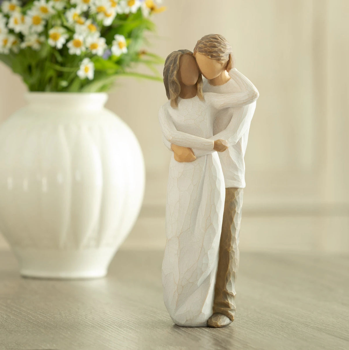 Front view of couple, standing with arms around each other. Woman has darker skin and hair; man has lighter skin and hair. Vase of flowers in background.