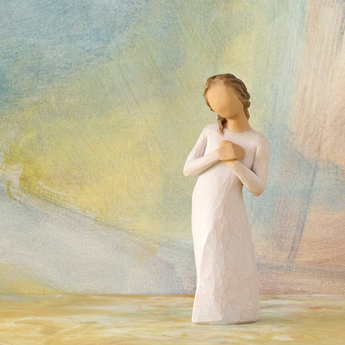 Willow Tree Here for You, 5”h hand-painted standing figure in cream dress, hands to heart in empathetic gesture, in front of ochre-green painting