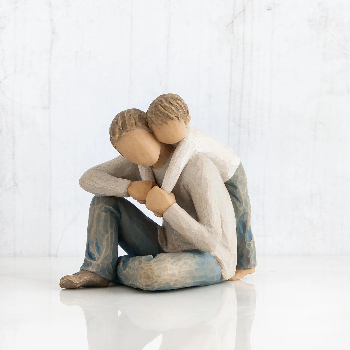Faceless man figurine sitting with young boy hugging him over his shoulders - wearing white shirts and blue jeans - all white background