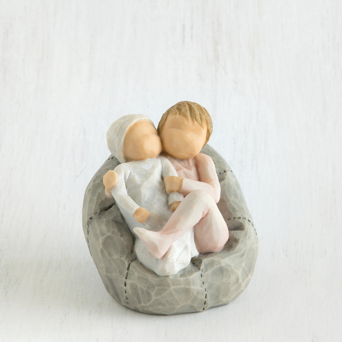 Two small baby figurines hugging another laying on grey beanbag