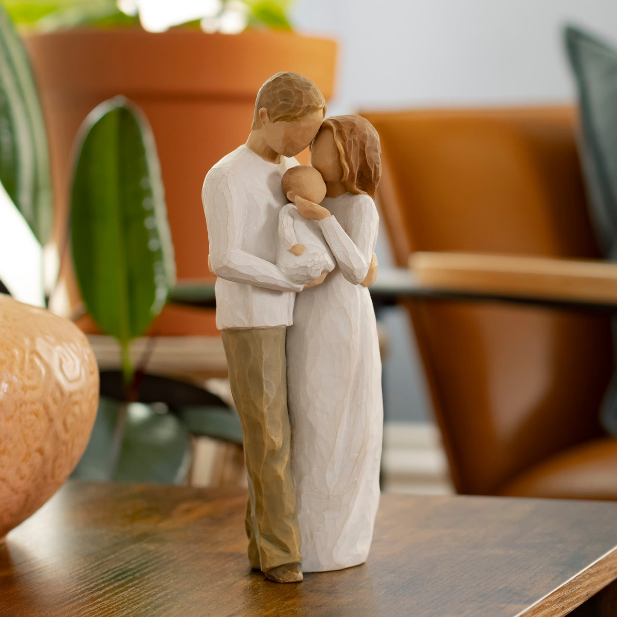Willow Tree Our Gift, 8.5”h hand-painted resin figure of standing couple holding baby between them, all in neutral clothing, on wooden table