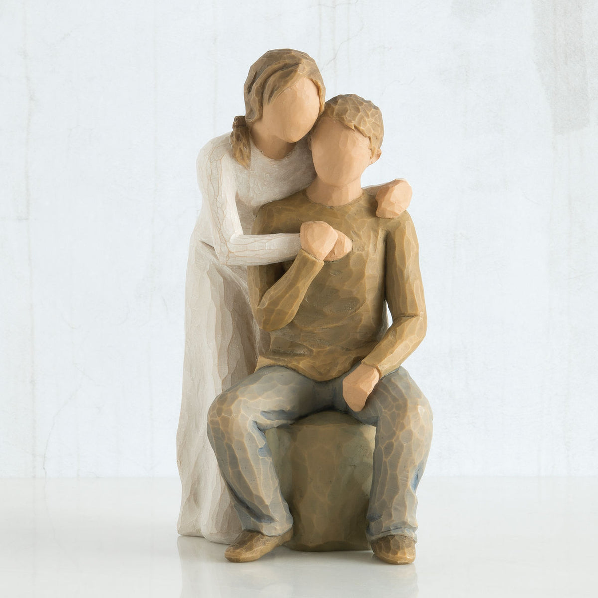 Faceless man figurine sitting on rock with faceless woman figurine over his shoulder holding one hand in all white