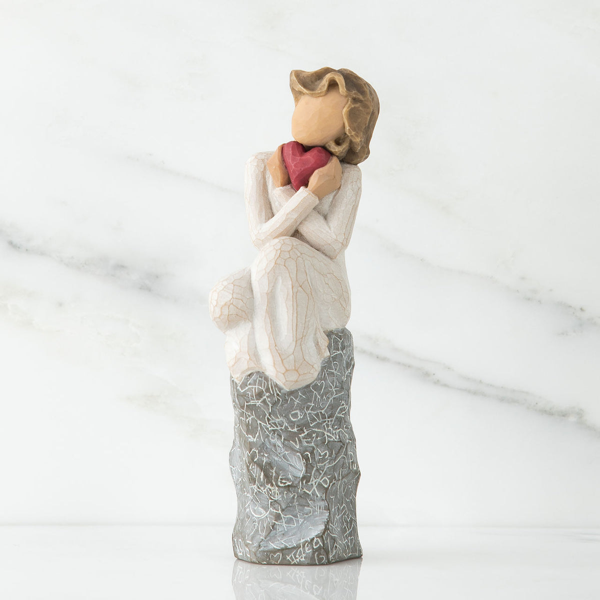 Young faceless little girl sitting on silver rock - she is wearing white and holding pink heart