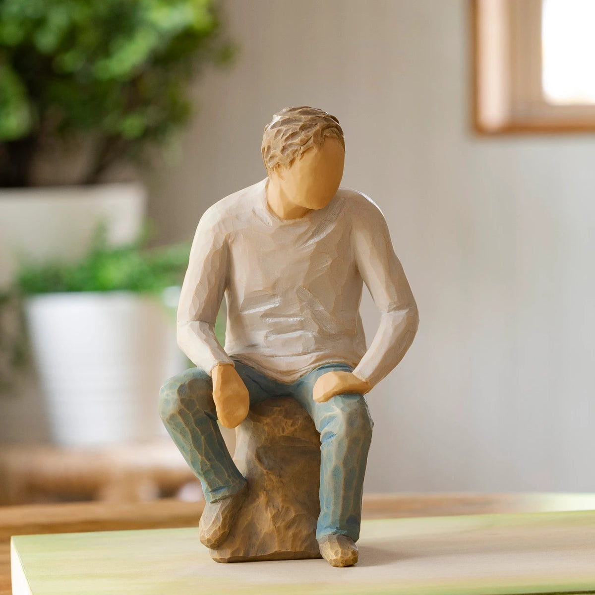 Willow Tree My Guy, 6”h hand-painted resin adult figure in light gray shirt and jeans, seated on gray rock, on wooden table