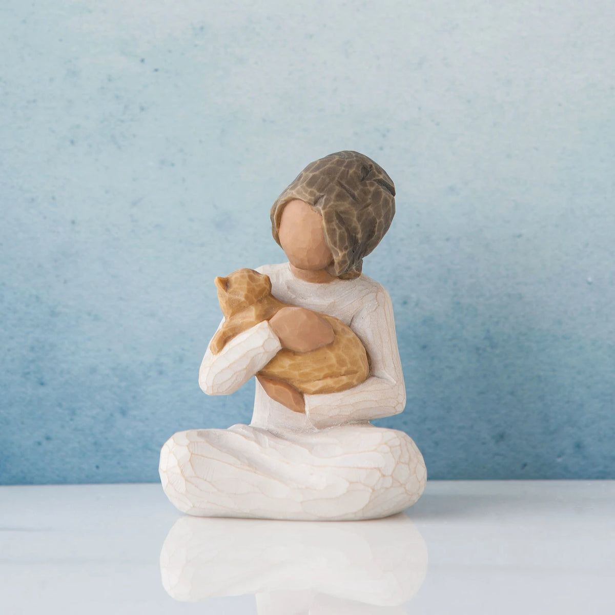 Small faceless girl figurine sitting down holding golden cat in her arms