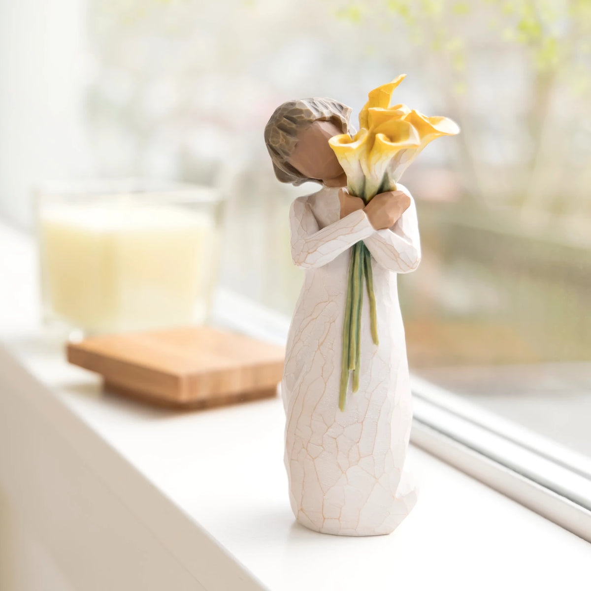Willow Tree With Gratitude, 5.5”h hand-painted resin figure with darker skin and hair, in cream dress, standing, holding bouquet of yellow calla lilies, on bright windowsill