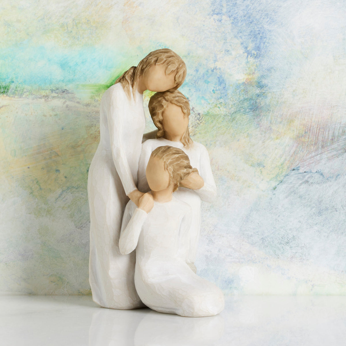 Willow Tree Our healing touch, 6.5”h hand-painted resin figure of three women; one standing with arm around kneeling girl, holding hand of seated girl, kneeling girl arranging hair of seated girl, all in cream dresses, in front of pastel painting