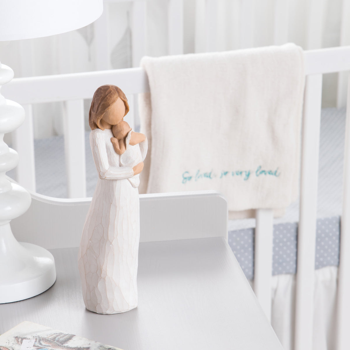 Front view of brunette woman figurine in white dress holding baby on white table