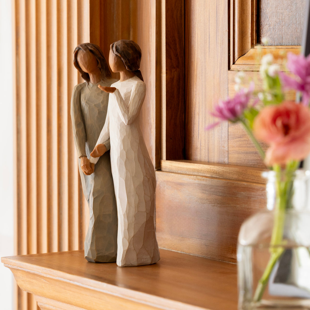 Willow Tree My sister, my friend, 8.5”h hand-painted standing figure of two women with darker skin and hair, standing arm in arm, one in cream dress, one in blue dress, on wooden shelf