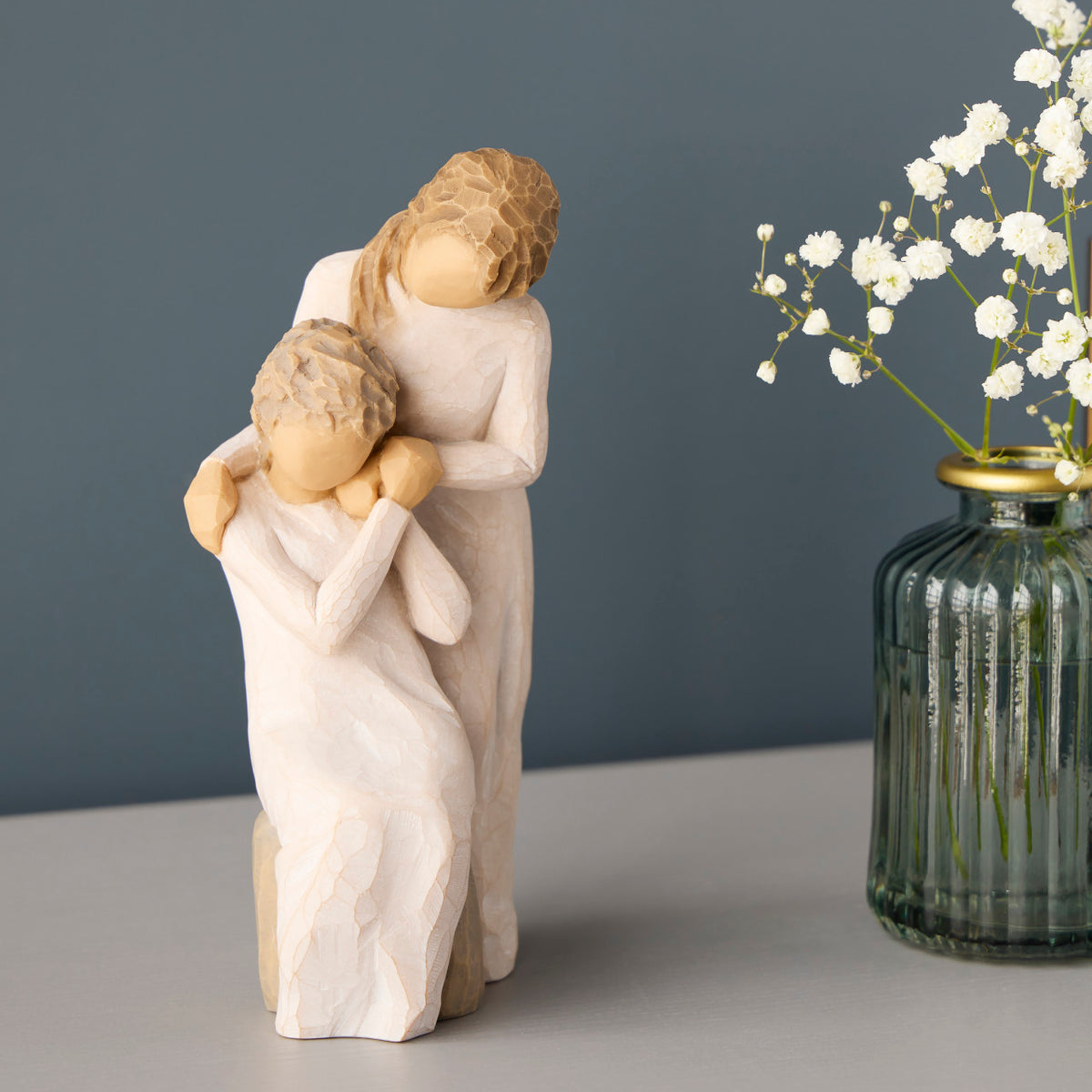 Willow Tree Loving My Mother, 6.5”h hand-painted resin figure of seated older woman with younger woman standing at her shoulder, both in cream dresses, hands clasped, on table with white flowers