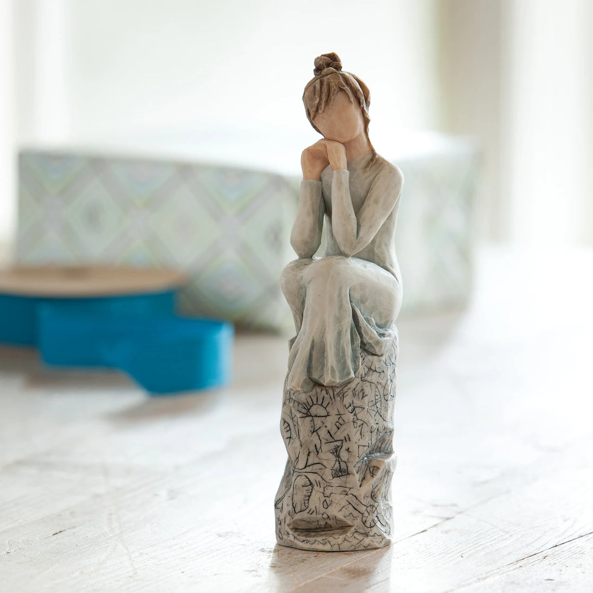 Willow Tree Patience, 7”h hand-painted resin figure in blue/gray dress, hands under chin, sitting on grey rock etched with symbols, on desk by window