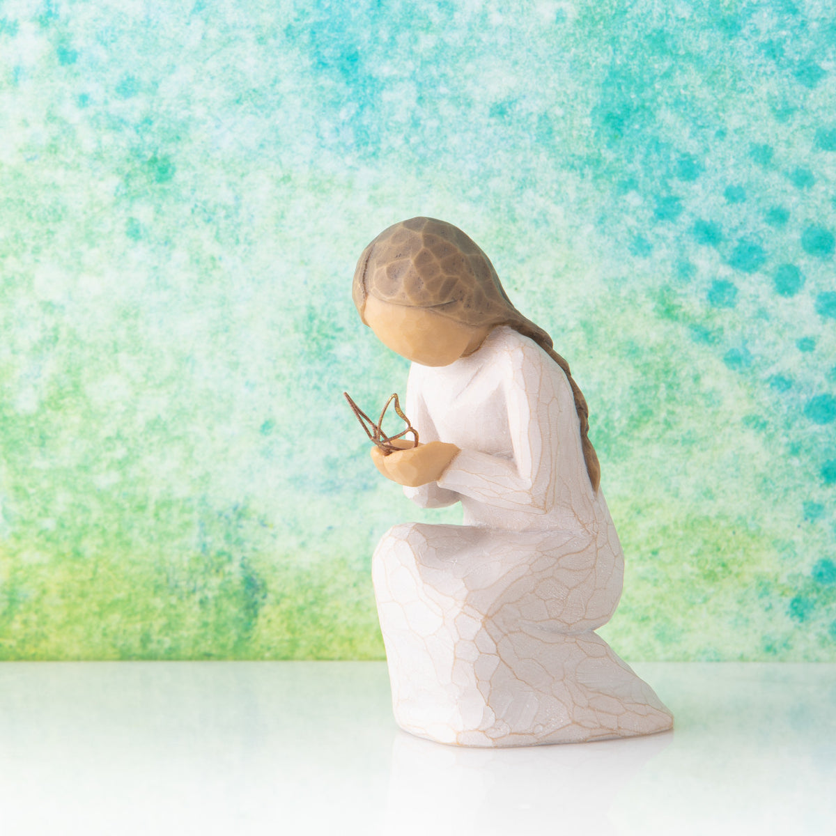 Willow Tree Quiet Wonder, 3.5”h hand-painted resin figure, kneeling in cream dress with gold leaf wire butterfly on extended hands, in front of blue green painting