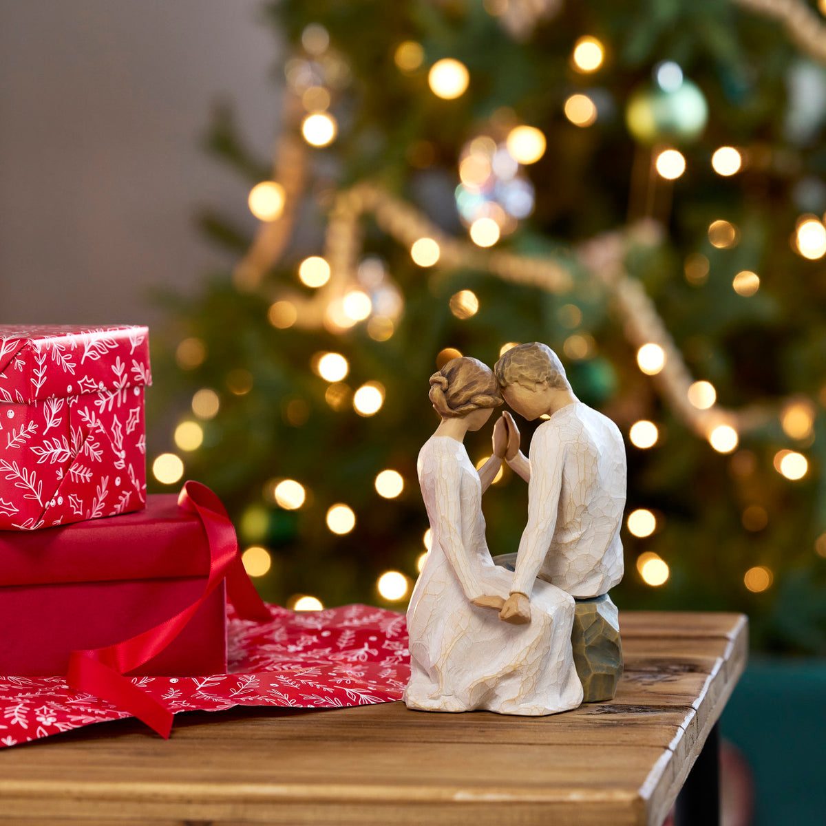 Willow Tree Around You, 6.5”h hand-painted figure of couple seated across from each other, heads and hands together, both in neutral clothing, on table by lit Christmas tree